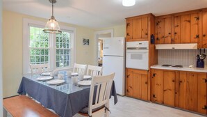 A dining area with a table set for four, wooden cabinets, a refrigerator, and a window with a view of greenery. - Minutes to Nantucket Sound Beaches! (South Yarmouth)
