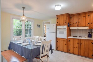 A dining area with a table set for four, wooden cabinets, a refrigerator, and a window with a view of greenery. - Minutes to Nantucket Sound Beaches! (South Yarmouth)