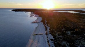 An aerial view of a coastal landscape with a road running parallel to the shoreline, surrounded by vegetation and leading to a body of water.