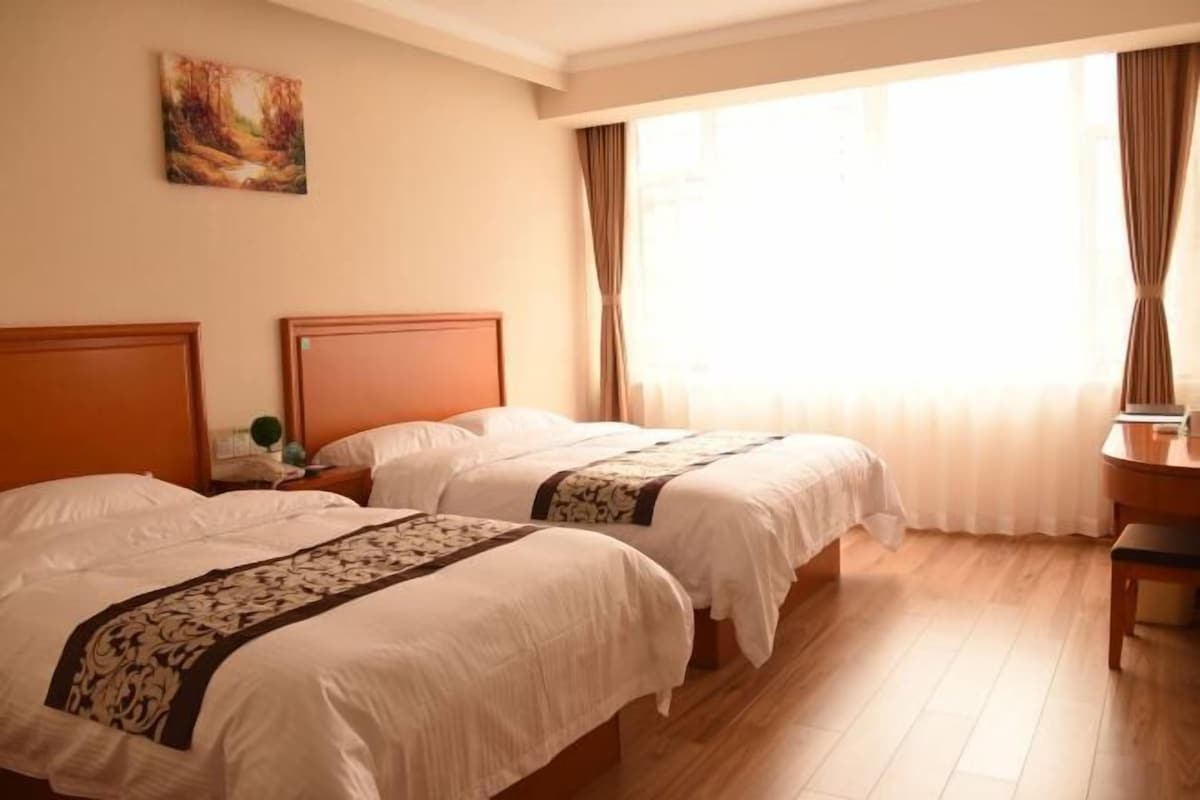 A hotel room with two beds, a desk, and a large window with curtains.