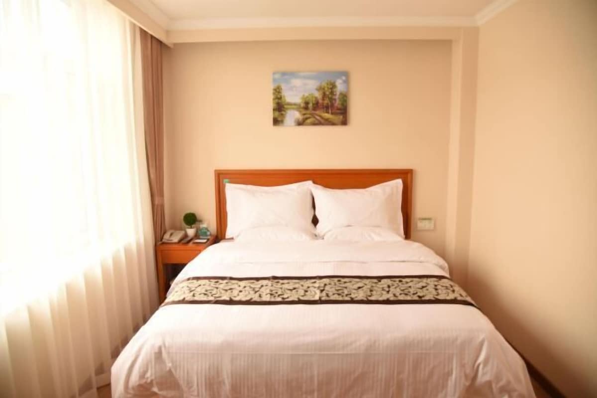 A hotel room with a bed, a nightstand, a painting on the wall, and a window with curtains.