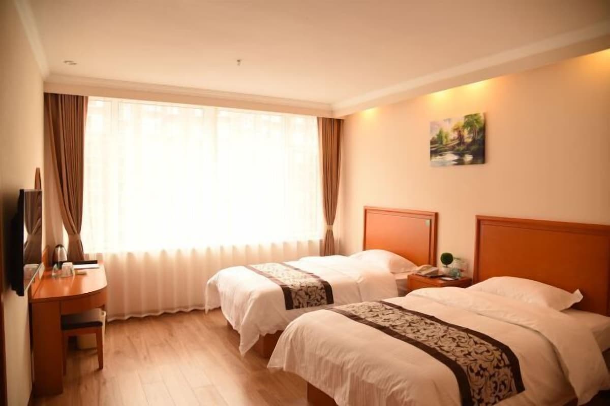 A hotel room with two beds, a desk, a chair, a TV, and a painting on the wall.