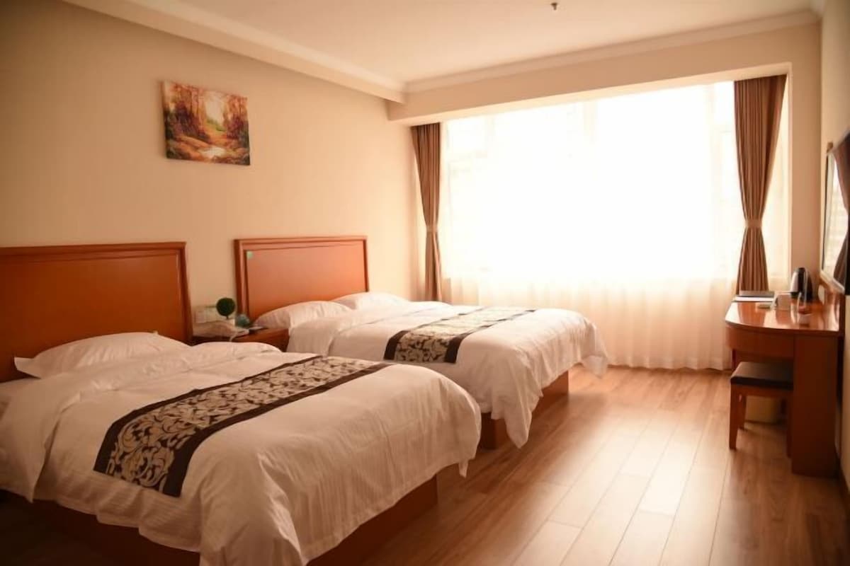A hotel room with two beds, a desk, a chair, a painting on the wall, and a large window with curtains.