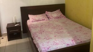 Een slaapkamer met een bed, een nachtkastje, een airconditioner en een lichtschakelaar op de muur.