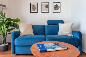Un canapé bleu avec deux coussins, une plante en pot et une table basse avec des livres.
