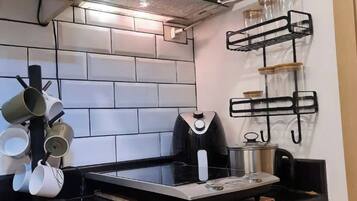 A kitchen with wooden cabinets, a black countertop, a stainless steel range hood, and a wall-mounted rack with kitchen utensils.