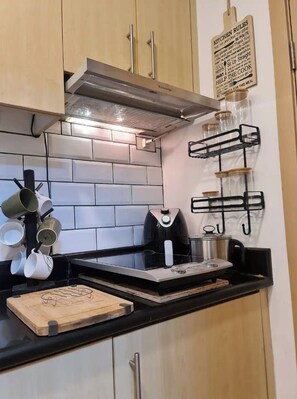 Eine Küche mit Holzausstattung, einer schwarzen Arbeitsplatte, einer Edelstahl-Dunstabzugshaube und einem an der Wand befestigten Küchenutensilienhalter.