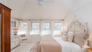 A bedroom with a bed, a dresser, a bench, and a ceiling fan. - Private Pool + Whimsical Sleeping Porch Steps from Beach by Tybee Cottages (Tybee Island)