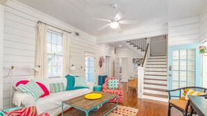 A spacious living room with a wooden coffee table, a sofa, and a chair. A staircase leads to an upper level. - Private Pool + Whimsical Sleeping Porch Steps from Beach by Tybee Cottages (Tybee Island)