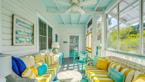 A bright, sunlit room with striped yellow and white furniture, a ceiling fan, and large windows offering a view of greenery outside. - Private Pool + Whimsical Sleeping Porch Steps from Beach by Tybee Cottages (Tybee Island)
