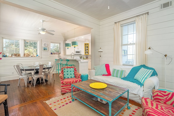 A spacious living room with a wooden coffee table, a sofa with colorful cushions, and a dining area with a white table and chairs.