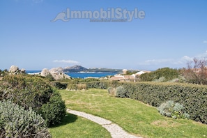 A landscaped garden with a stone pathway leading to a scenic view of the sea and mountains. - Amazing sea view (Santa Teresa Gallura)