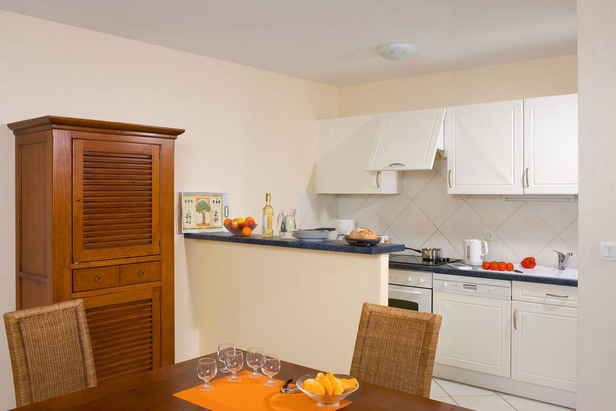 Una cocina compacta con alacenas blancas, un mueble de madera y una mesa de comedor con sillas.