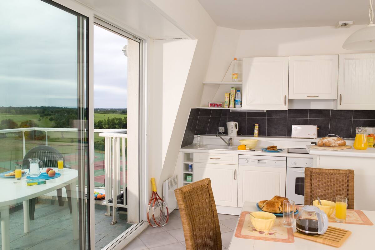 Una cocina moderna con armarios blancos, un salpicadero negro y una zona de comedor con una mesa dispuesta para el desayuno.