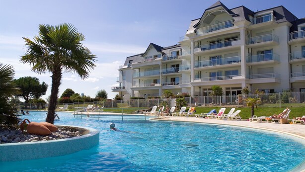A swimming pool with lounge chairs and a palm tree, surrounded by a multi-story hotel building. - Résidence Madame Vacances Les Appartements de Fontenelles (L'Aiguillon-sur-Vie)