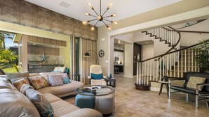 A spacious living area with a large sofa, ottomans, a glass coffee table, and a modern staircase.