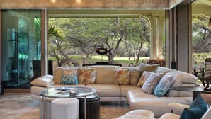 A modern living room with a sectional sofa, a glass coffee table, and a view of a garden through large windows.