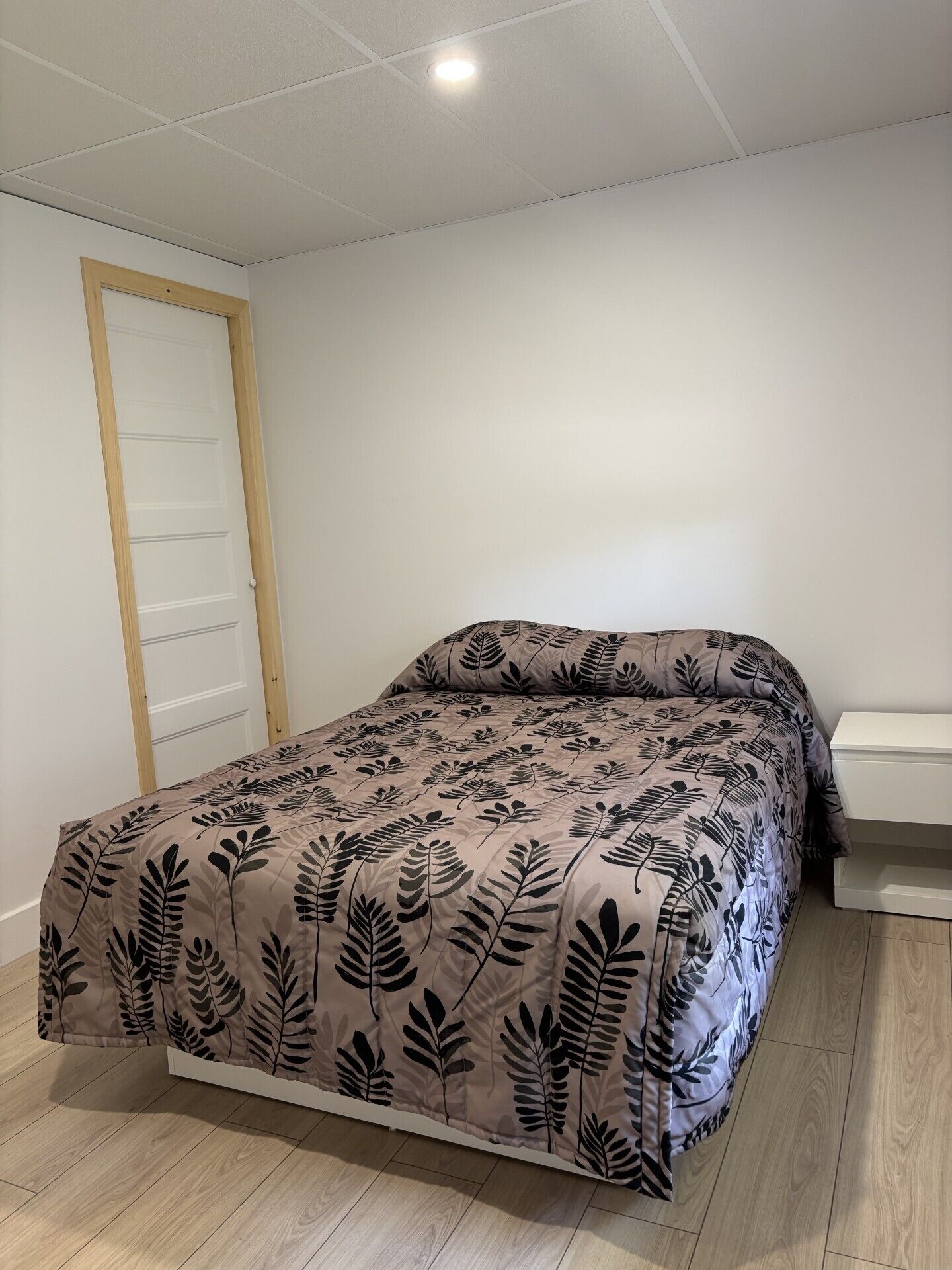 A bedroom with a bed, a wooden door, and a white bedside table.