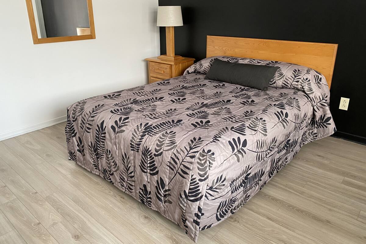 A bedroom with a bed, a nightstand, a lamp, and a mirror on the wall.