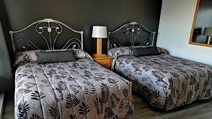 A double bed with a leaf-patterned bedspread, a nightstand with a lamp, and a mirror on the wall.