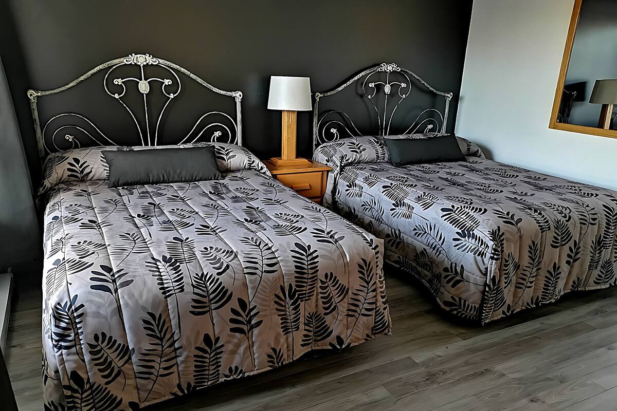 A double bed with a leaf-patterned bedspread, a nightstand with a lamp, and a mirror on the wall.