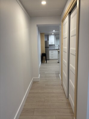 Un pasillo con piso de madera que conduce a una zona de cocina con armarios y un taburete.
