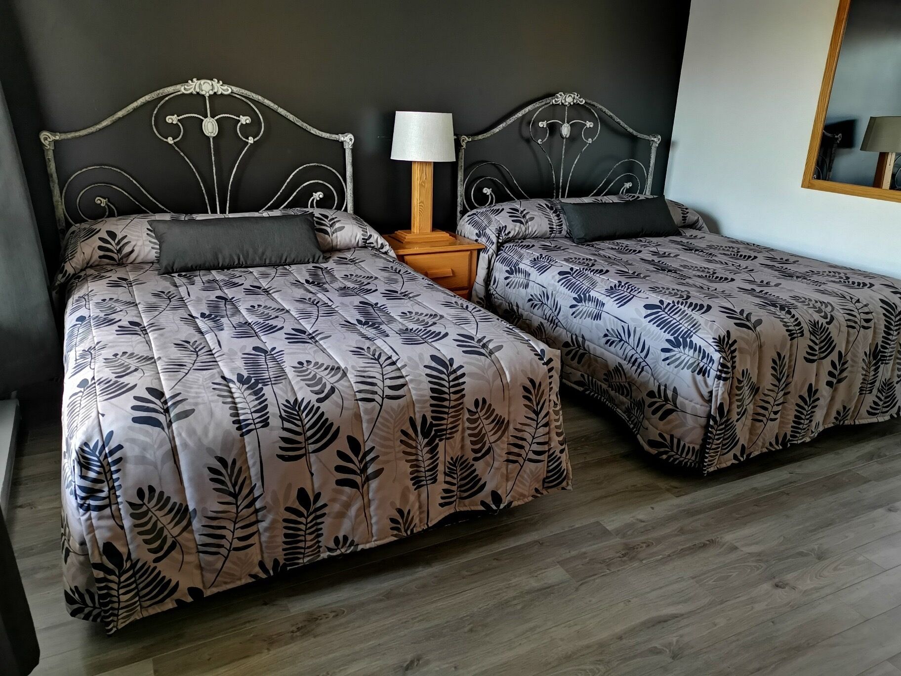 Una cama doble con una colcha estampada con hojas y una mesita de noche con una lámpara.