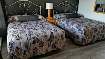 Una cama doble con una colcha estampada con hojas y una mesita de noche con una lámpara.