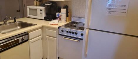 Una cocina compacta con un lavamanos de acero inoxidable, armarios blancos, un microondas, una estufa y un refrigerador.