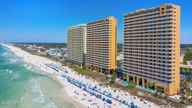 Un hotel frente a la playa con varios edificios altos, una playa arenosa con sombrillas y un cielo azul despejado.