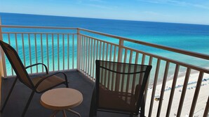 Un balcón con dos sillas y una mesa, con vista a una playa de aguas turquesas cristalinas y una costa distante.