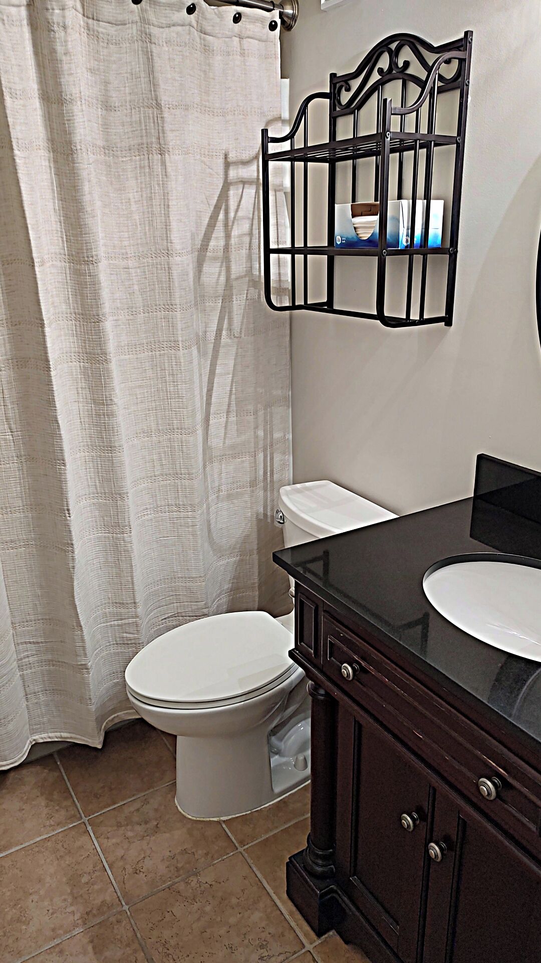 A bathroom with a white toilet, a black vanity with a mirror, and a shower curtain.