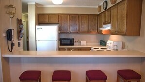 A kitchen with wooden cabinets, a refrigerator, a microwave, and a coffee maker. There are three stools with red cushions. - 2116  Mystic Mountain View - Hot tub, sauna & more resort amenities (Beech Mountain)
