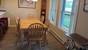 A dining room with a wooden table and chairs, a chandelier, and a view of the outdoors through large windows. - 2116  Mystic Mountain View - Hot tub, sauna & more resort amenities (Beech Mountain)