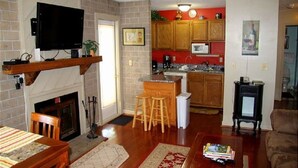 A living room with a fireplace, a television, a dining area, and a kitchen with wooden cabinets and a red wall. - 4216  Hot tub, sauna & more resort amenities  Northview Retreat (Banner Elk)