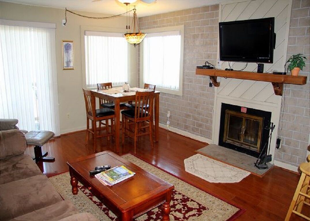 A living room with a wooden dining table, chairs, a sofa, a fireplace, and a mounted TV.