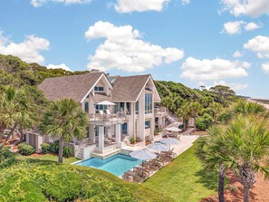 A large two-story house with a swimming pool, outdoor seating, and lush landscaping.