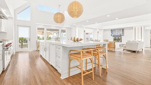 Una cocina amplia con una isla grande, piso de madera y lámparas colgantes de mimbre.