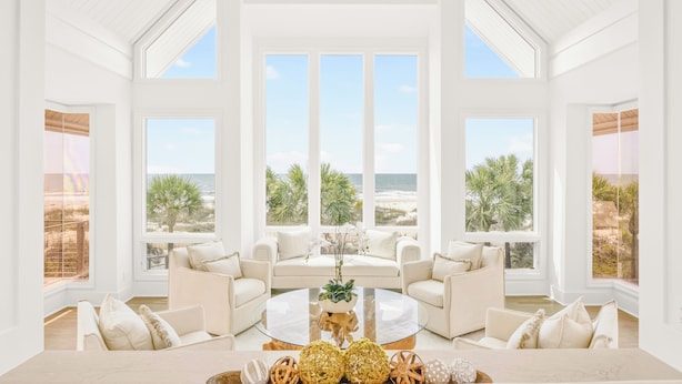 Una habitación amplia con ventanas grandes, una mesa de centro redonda de cristal y dos sofás blancos.