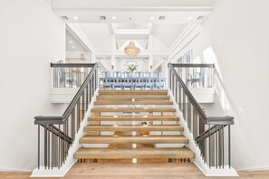 A staircase with wooden steps and black railings, leading to a dining area with blue chairs and a chandelier.