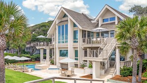 Una casa de varios pisos con piscina, mobiliario exterior y una escalera que lleva a un balcón.