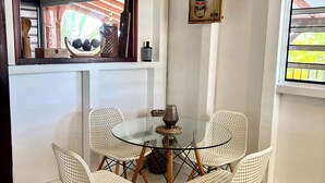 A dining area with a glass table surrounded by four white chairs with wooden legs. A decorative bowl and a candle are on the table. - Modern Surf'Kreol villa 3 min from Le Souffleur - Fibre - Swimming pool (Port-Louis)