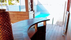 A wooden deck with a curved table, a woven basket, and a view of a pool. - Modern Surf'Kreol villa 3 min from Le Souffleur - Fibre - Swimming pool (Port-Louis)