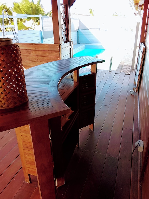 A wooden deck with a curved table, a woven basket, and a view of a pool.
