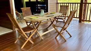 A wooden deck with a table and chairs, a hanging light fixture, and a view of greenery through the windows. - Modern Surf'Kreol villa 3 min from Le Souffleur - Fibre - Swimming pool (Port-Louis)