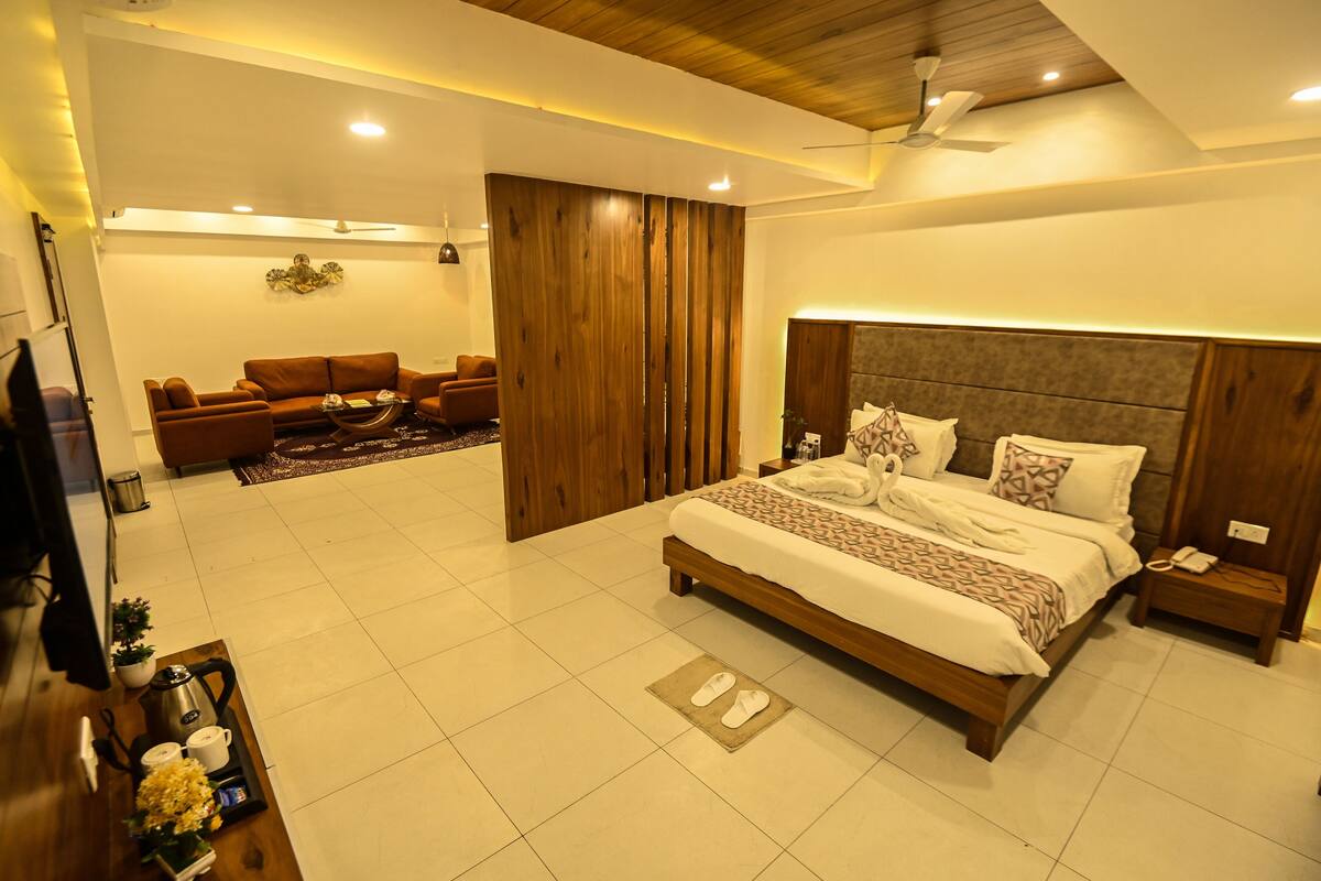 A modern bedroom with a large bed, a wooden headboard, a bedside table with a phone, and a TV on a stand.
