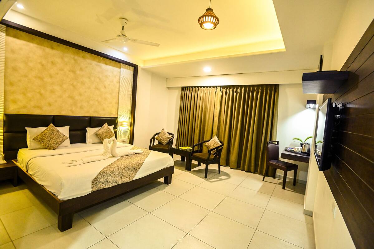 A hotel room with a large bed, a desk with a chair, a television, and a ceiling fan.