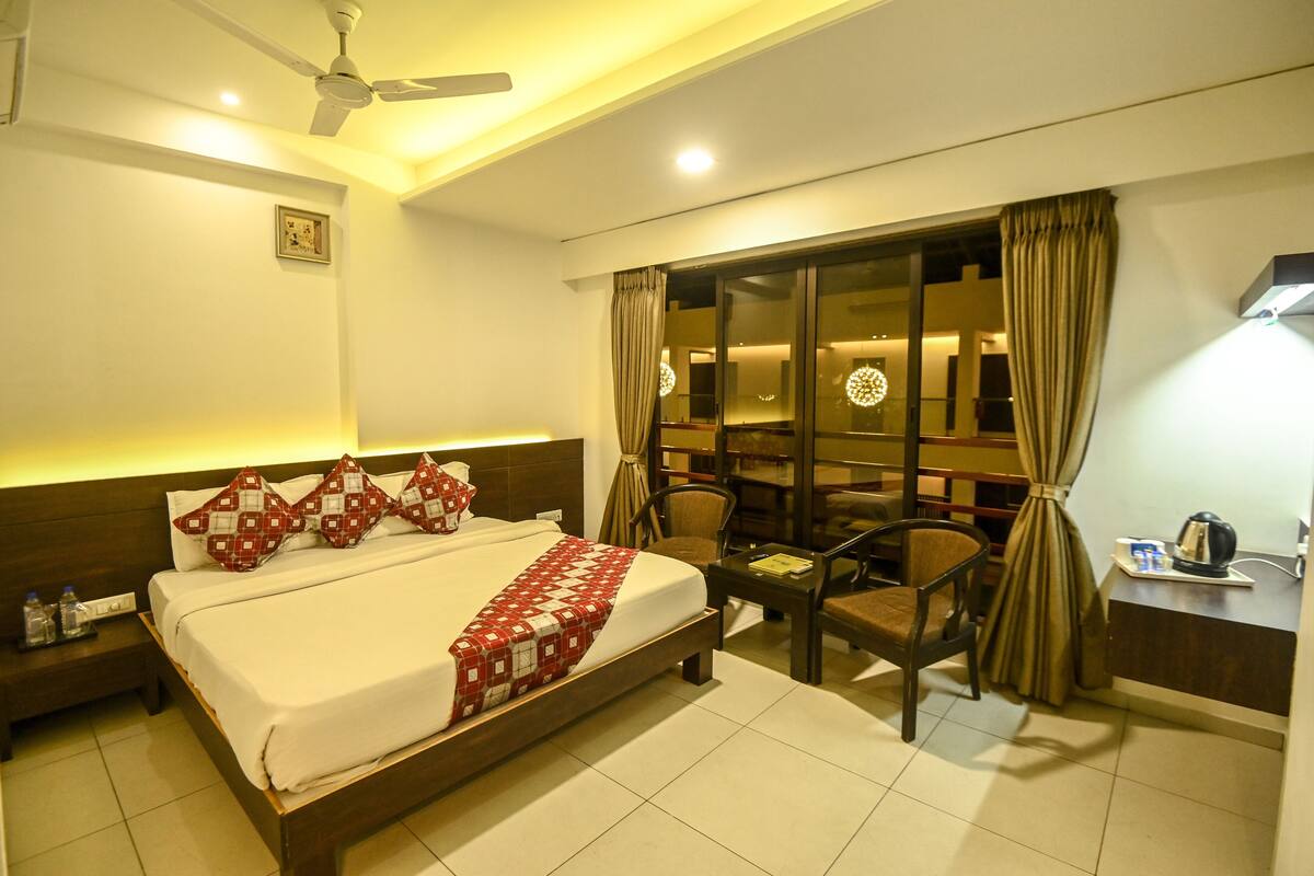 A hotel room with a bed, a desk, a chair, a ceiling fan, and a window with curtains.