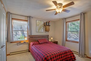Ein Schlafzimmer mit einem Bett, Deckenventilator, Nachttisch, Lampe und einem Fenster mit Jalousien.