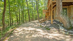 A wooden cabin with a gravel path leading to a wooden deck, surrounded by a forest.